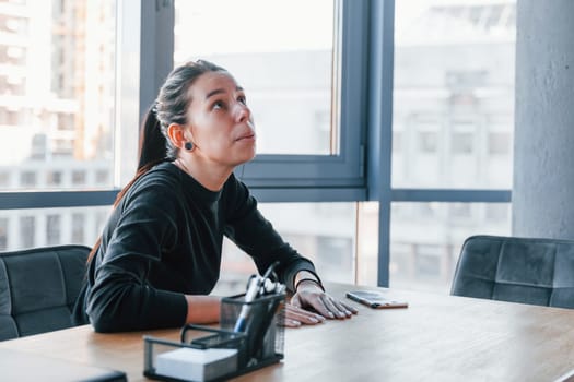 Woman in black formal clothes is indoors in the modern office.