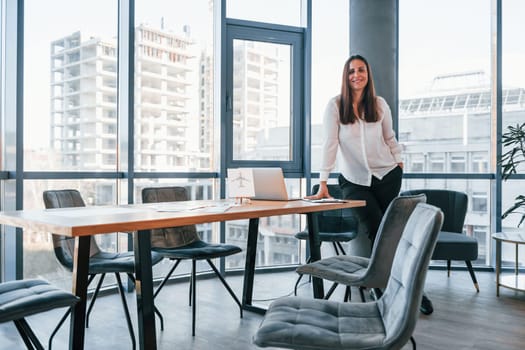 Young woman in white formal clothes is indoors in the modern office.