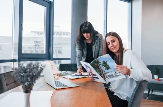 Two women in formal clothes is indoors in the modern office works together.