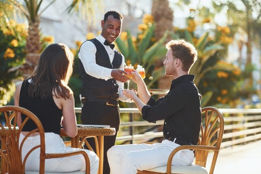 Serviced by waiter. Happy young couple is together on their vacation. Outdoors at sunny daytime.