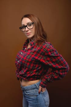 Young attractive woman in a plaid shirt and cat-eye glasses smiles playfully. Beautiful female model, brunette posing.