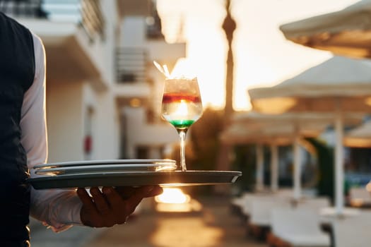 Close up view of drink. Black waiter in formal clothes is at his work outdoors at sunny daytime.