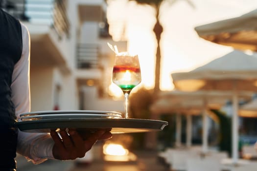 Close up view of drink. Black waiter in formal clothes is at his work outdoors at sunny daytime.