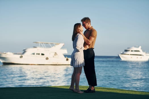 Sea and yacht at background. Happy young couple is together on their vacation. Outdoors at sunny daytime.