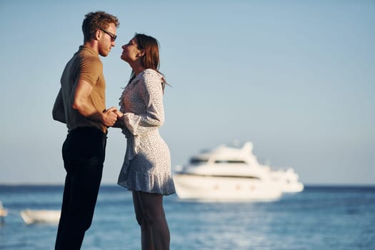 Sea and yacht at background. Happy young couple is together on their vacation. Outdoors at sunny daytime.