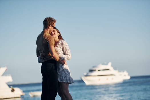 Sea and yacht at background. Happy young couple is together on their vacation. Outdoors at sunny daytime.