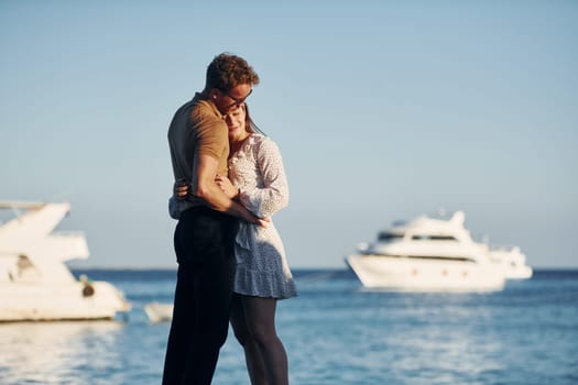 Sea and yacht at background. Happy young couple is together on their vacation. Outdoors at sunny daytime.