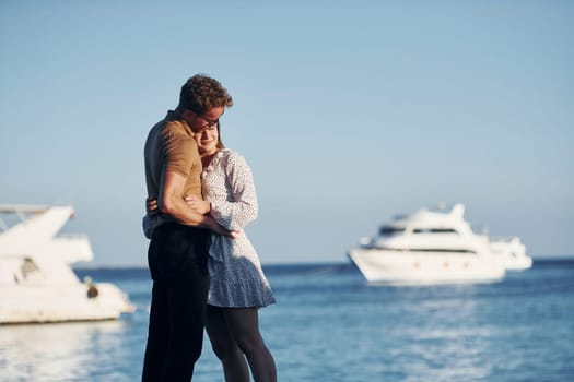 Sea and yacht at background. Happy young couple is together on their vacation. Outdoors at sunny daytime.