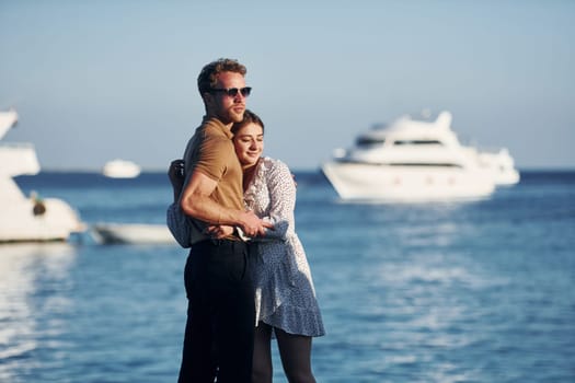 Sea and yacht at background. Happy young couple is together on their vacation. Outdoors at sunny daytime.
