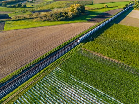 A modern InterCityExpress between fields in the countryside seen from a drone perspective