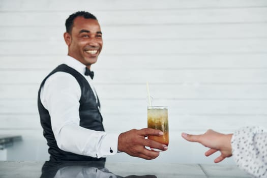 With order in hand. Black waiter in formal clothes is at his work outdoors at sunny daytime.