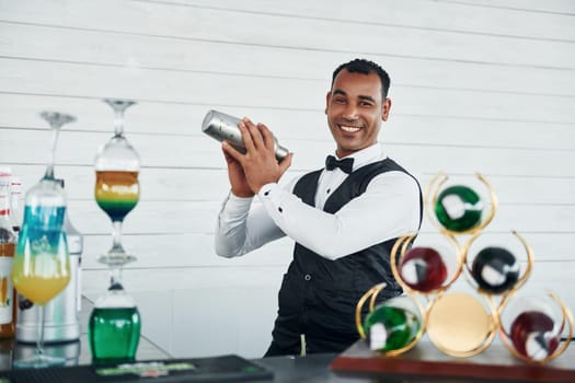 At the bar. Black waiter in formal clothes is at his work outdoors at sunny daytime.