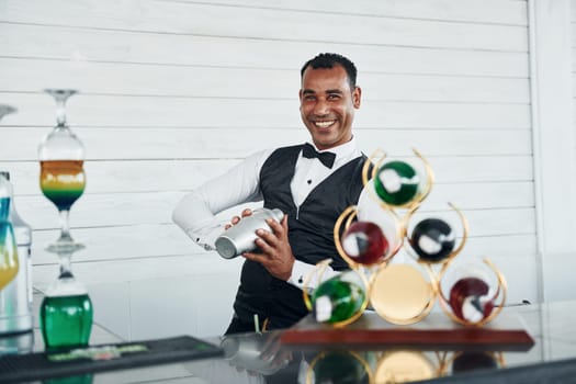 At the bar. Black waiter in formal clothes is at his work outdoors at sunny daytime.