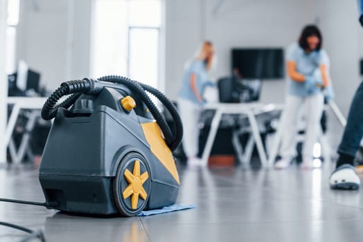 Woman uses vacuum cleaner. Group of workers clean modern office together at daytime.