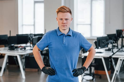 Portrait of young man in blue shirt and black protective gloves. Standing in the office.