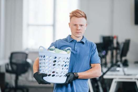 Portrait of young man in blue shirt and black protective gloves. Standing in the office.