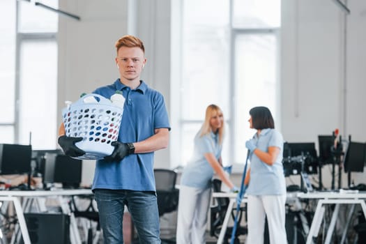 Woman uses vacuum cleaner. Group of workers clean modern office together at daytime.