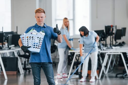 Woman uses vacuum cleaner. Group of workers clean modern office together at daytime.