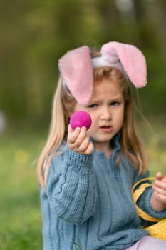 Girl with bunny ears collects chocolate eggs in a basket for Easter Focus on an egg