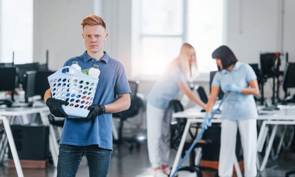 Woman uses vacuum cleaner. Group of workers clean modern office together at daytime.