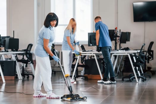 Woman uses vacuum cleaner. Group of workers clean modern office together at daytime.