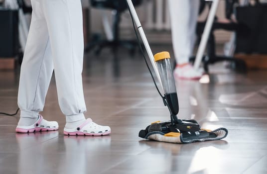 Close up view of woman that uses vacuum cleaner indoor in modern office.