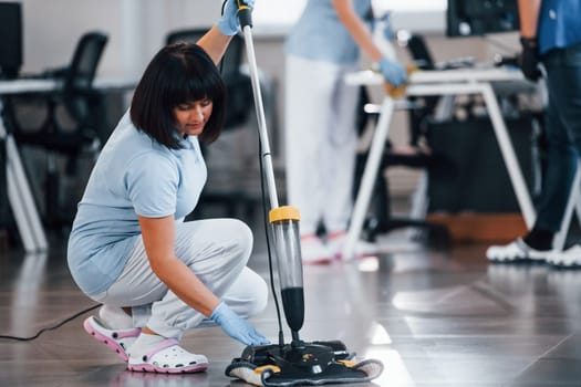 Woman uses vacuum cleaner. Group of workers clean modern office together at daytime.