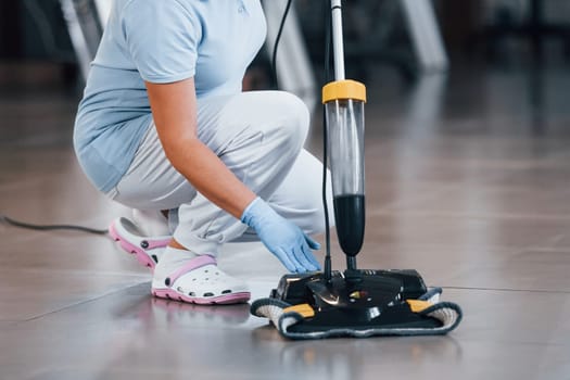 Close up view of woman that uses vacuum cleaner indoor in modern office.