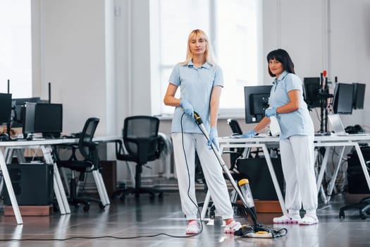 Woman uses vacuum cleaner. Group of workers clean modern office together at daytime.