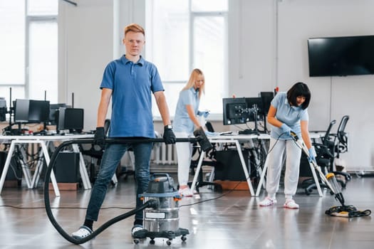 Guy with vacuum cleaner. Group of workers clean modern office together at daytime.