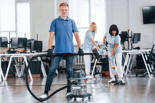 Guy with vacuum cleaner. Group of workers clean modern office together at daytime.