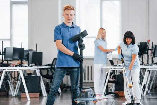 Guy with vacuum cleaner. Group of workers clean modern office together at daytime.