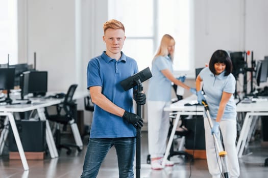 Guy with vacuum cleaner. Group of workers clean modern office together at daytime.
