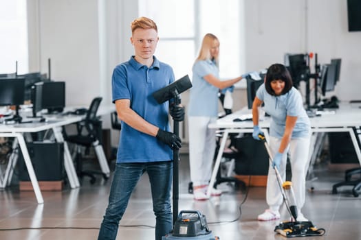 Guy with vacuum cleaner. Group of workers clean modern office together at daytime.