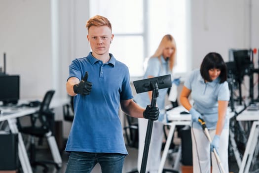 Guy with vacuum cleaner. Group of workers clean modern office together at daytime.