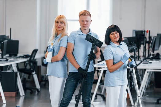 Guy with vacuum cleaner. Group of workers clean modern office together at daytime.