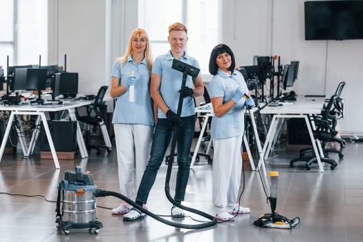 Guy with vacuum cleaner. Group of workers clean modern office together at daytime.