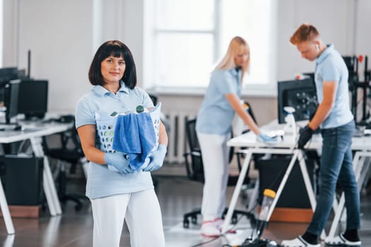 Woman with basket. Group of workers clean modern office together at daytime.