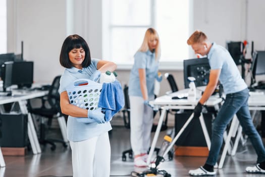 Woman with basket. Group of workers clean modern office together at daytime.