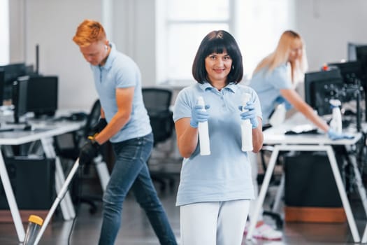 Group of workers clean modern office together at daytime.