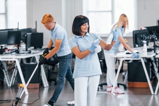 Group of workers clean modern office together at daytime.
