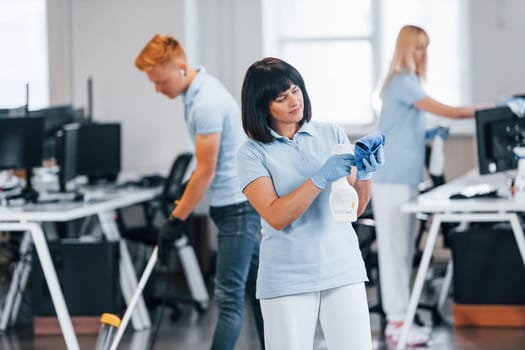 Cleans floor. Group of workers clean modern office together at daytime.