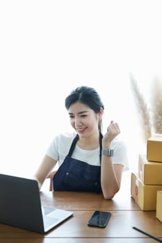 Starting small business entrepreneur of independent Asian woman smiling using laptop computer with cheerful success of online marketing package box items and SME delivery concept.