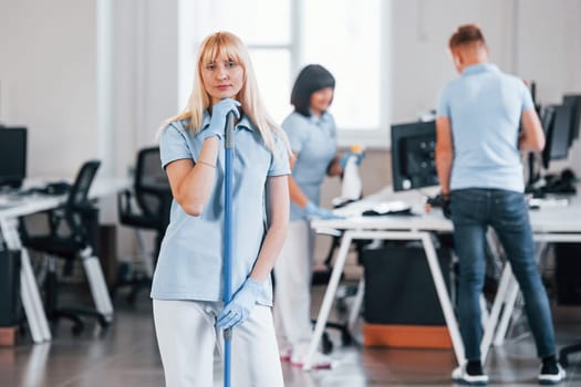 Cleans floor. Group of workers clean modern office together at daytime.