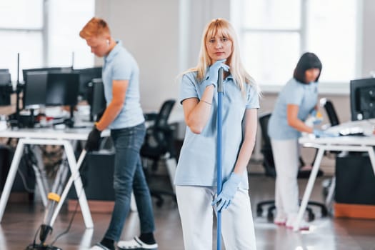 Cleans floor. Group of workers clean modern office together at daytime.