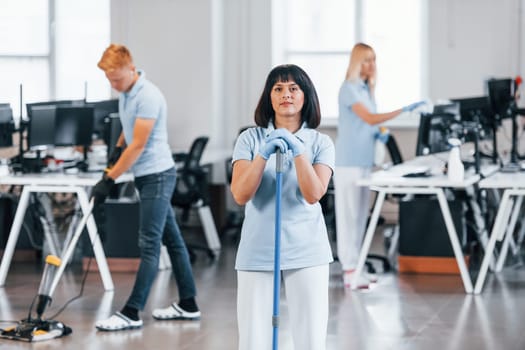 Cleans floor. Group of workers clean modern office together at daytime.