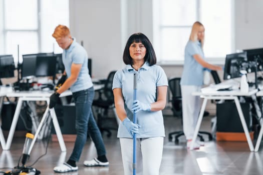 Cleans floor. Group of workers clean modern office together at daytime.