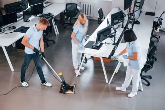 Cleans floor. Group of workers clean modern office together at daytime.