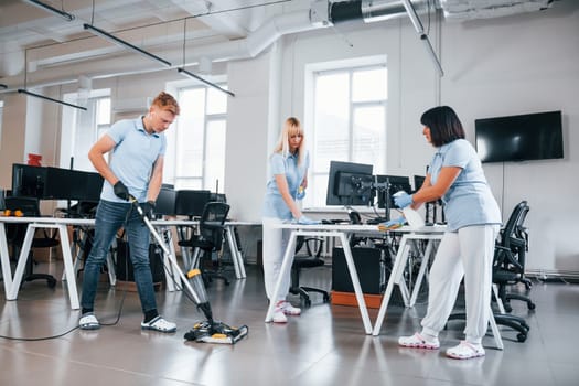 Cleans floor. Group of workers clean modern office together at daytime.