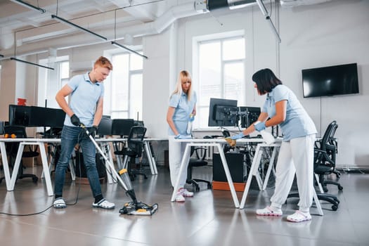 Cleans floor. Group of workers clean modern office together at daytime.